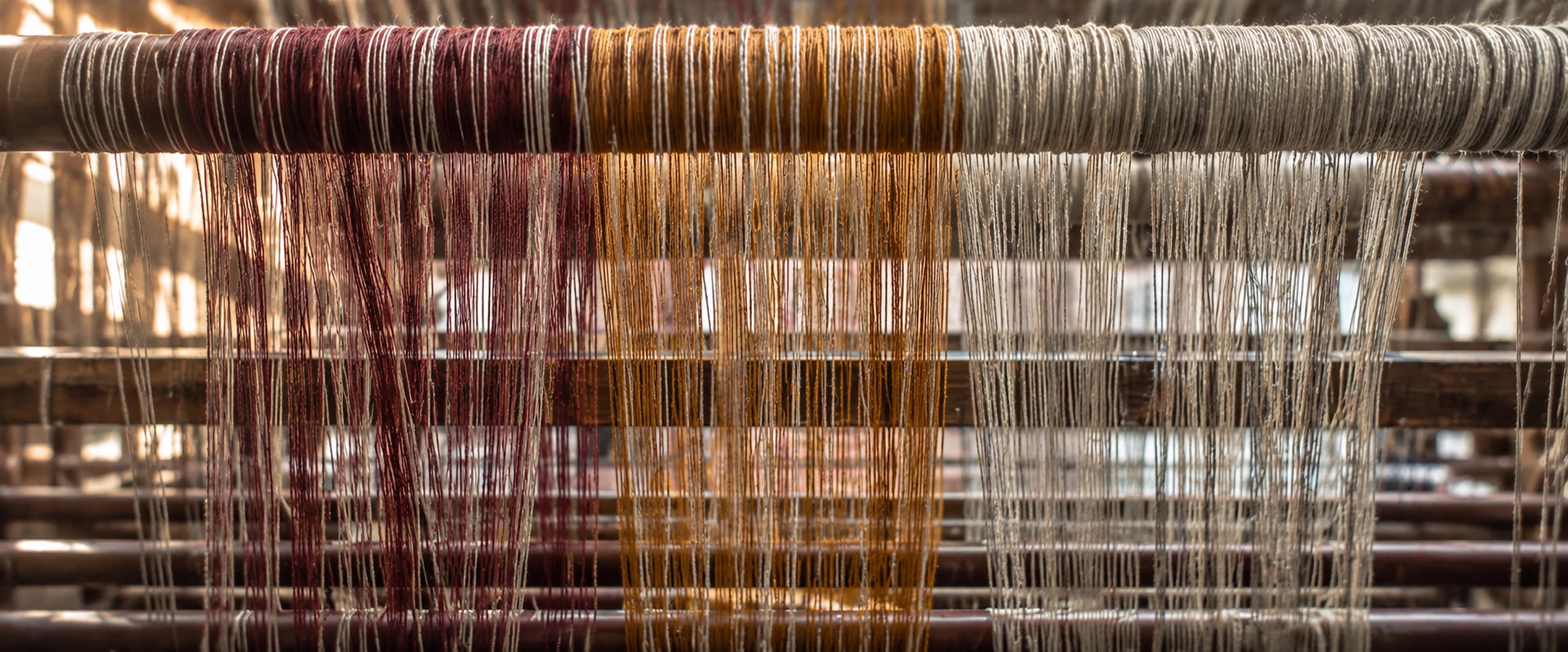 Burgundy, ochre, and natural yarns suspended across an artisan loom